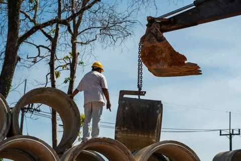Using an excavator to translate large pipes into a vehicle helping a person. Stock Photos