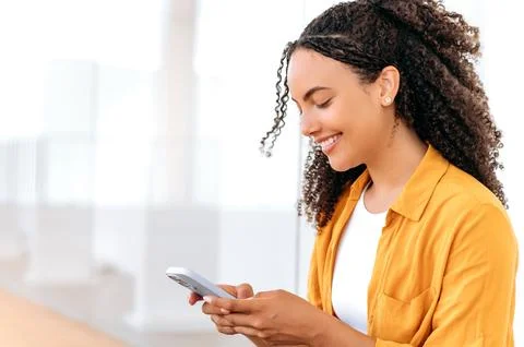 Using gadgets. Close-up side view photo of a pretty, curly haired hispanic or Stock Photos