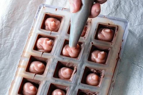 Using the icing nozzle to fill chocolate candies with ganache. Stock Photos