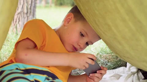 Using iphone. Child with iphone in tent on summer day. Kid and iphone Stock Footage 134737500