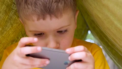 Using iphone. Child with iphone in tent on summer day. Kid and iphone Stock Footage 134738174