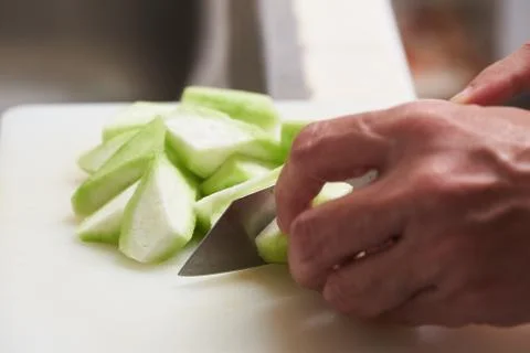 Using kitchen knife chopping zucchini on white board Stock Photos
