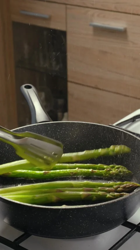 Using kitchen tongs to turn asparagus in a frying pan Stock Footage 335751760
