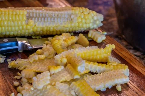 Using a knife to remove kernels from the cob of an ear of sweet corn. Stock Photos