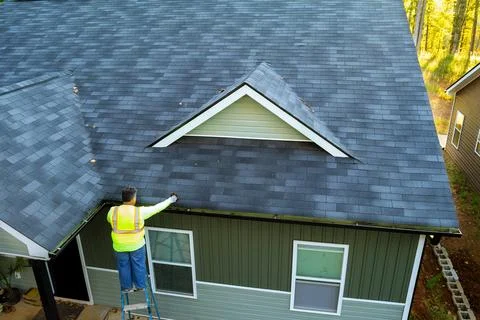 Using a ladder, worker cleans debris, dirt, fallen leaves from clogged roof Stock-Fotos