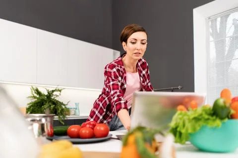 Using a laptop computer while cooking young housewife searching online recipes Stock Photos