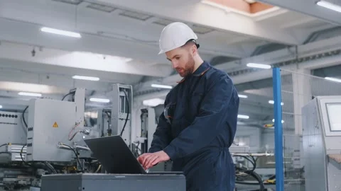 Using the laptop. Factory worker is indoors with hard hat. 動画素材 297477233