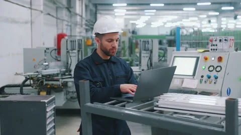 Using the laptop. Factory worker is indoors with hard hat. 動画素材 297477325