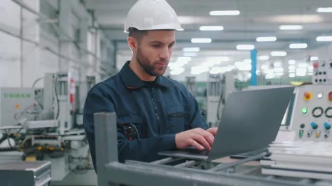 Using the laptop. Factory worker is indoors with hard hat. 動画素材 297477360