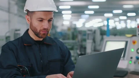 Using the laptop. Factory worker is indoors with hard hat. 動画素材 297477380