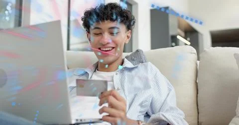 Using laptop, man in blue-striped shirt holding credit card, sitting on beige Foto stock