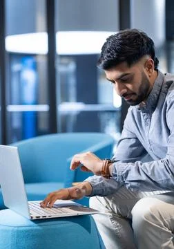 Using laptop, man checking time on smartwatch while working in modern office, Foto stock