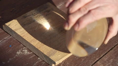 Using a magnifying glass and sunlight, burning occurs on a wooden surface Stock Footage 305329689