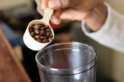 Using a measuring spoon, place the coffee beans into the coffee mill Stock Photos
