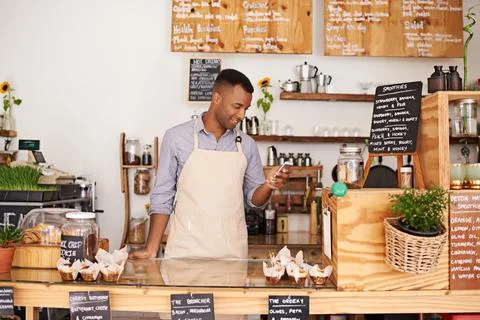Using a mobile app to organize tasks for his shift. young barista using a phone Stock Photos