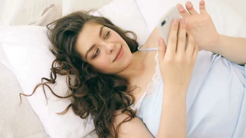 Using mobile cellphone in bed. Chatting relaxed mood. Woman in sunny bedroom Vídeo Stock 90049373