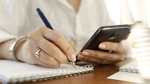  Using a mobile phone. A girl writes information from a smartphone in a notebook Video stock 110722441