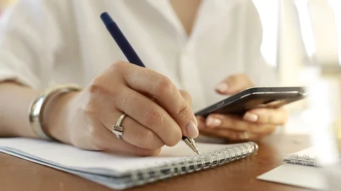  Using a mobile phone. A girl writes information from a smartphone in a notebook Video stock 110722499