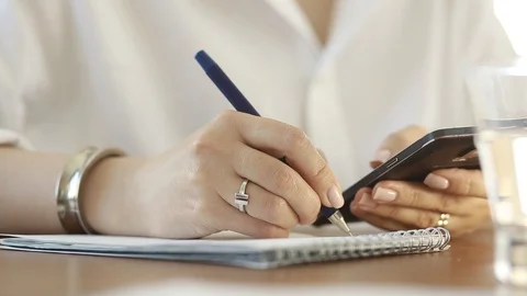  Using a mobile phone. A girl writes information from a smartphone in a notebook Video stock 110722501