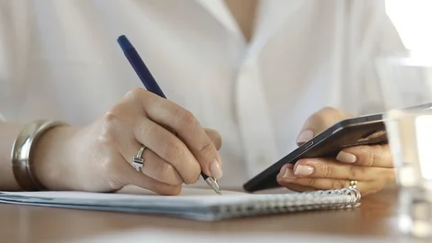  Using a mobile phone. A girl writes information from a smartphone in a notebook Video stock 110722522