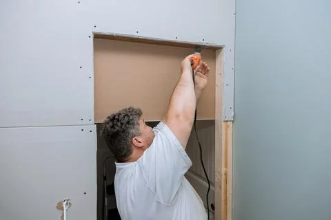 Using a multi tool worker cuts the drywall plasterboard with a cutting blade Stock Photos