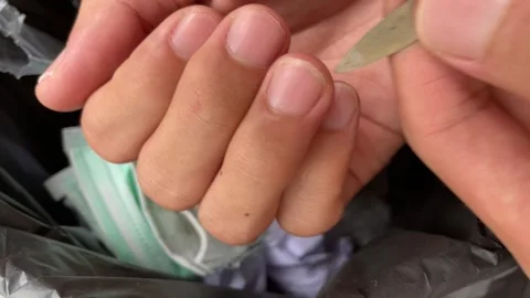 Using nail polishing tool to clean dirt from nail with blurred trash inside bin. Stock Footage 249587358