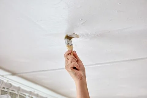 Using paintbrush to touch up ceiling with white paint, house painter paints.. Stock Photos