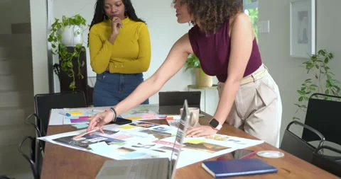 Using photos and notes, diverse female coworkers are arranging board at table Stock Footage 336957698