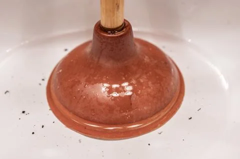 Using a plunger on a bathroom sink plugged with Hair and scum in a pool of Stock Photos