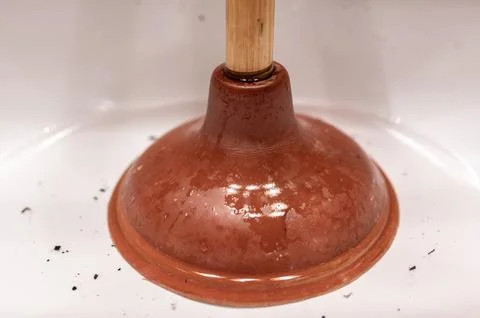 Using a plunger on a bathroom sink plugged with Hair and scum in a pool of Stock Photos