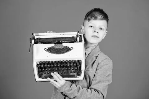Using retro technology. Little boy holding retro typewriter on blue background Stock Photos