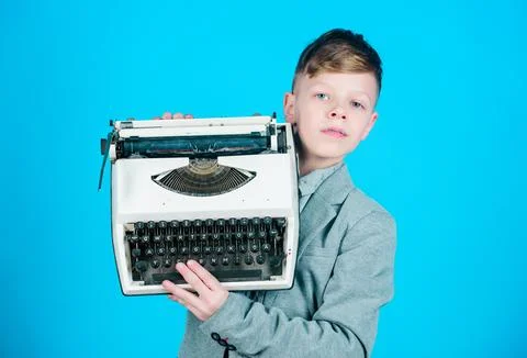 Using retro technology. Little boy holding retro typewriter on blue background Stock Photos