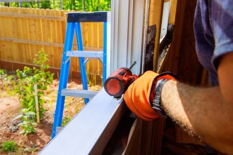 Using screwdriver, construction worker installs window in a new home 스톡 사진