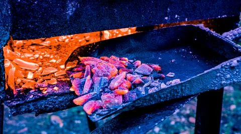Using a shovel to bring the coals to the flame inside the grill Stock Photos
