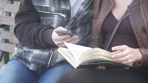 Using a smartphone and reading a book outdoors Stock Footage 88863518