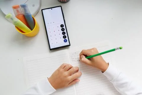 Using a smartphone calculator to complete math homework and write answers in Stock Photos