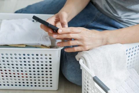 Using a smartphone during a home laundry routine. People check messages besid Stock Photos