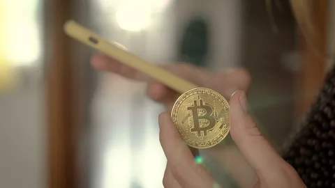 Using a smartphone with a hand and holding a bitcoin coin with the other Stock Footage
