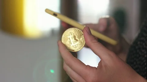 Using a smartphone with a hand and holding a bitcoin coin with the other Video stock 92921190