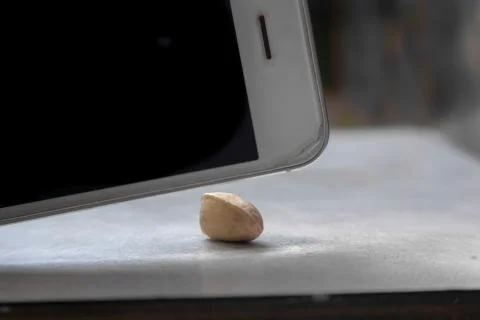 Using smartphone as nut chopper. phone nutcracker. Phone and nut. Unusual using Фото