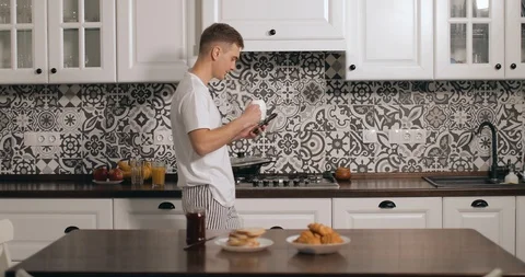 Using Smartphone while Drinking Coffee in Kitchen Видео 103825475