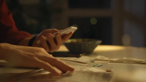 Using a smartphone while organizing documents in a dimly lit room at night Stock Footage 293733855