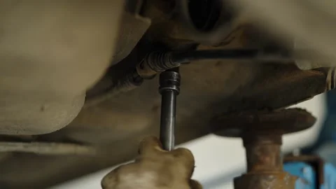 Using a socket wrench extension to unscrew a bolt under a car on a lift Stock Footage 337890997