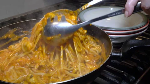 Using spoons to lift a portion of linguine pasta and sauce from pan to bowl. Video stock 168605760