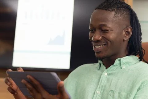 Using tablet, man smiling while analyzing financial data on screen in office Stock Photos