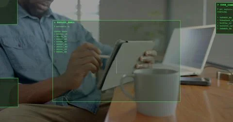 Using tablet with stylus, denim-shirted man working in home office with laptop Stockfoto's