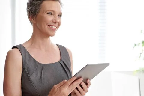 Using tech to her advantage. A mature businesswoman looking thoughtful while Stock Photos