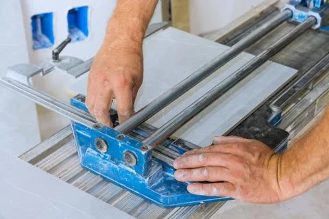 Using tile cutting hand machine, a construction worker cuts ceramic tile. Stock Photos