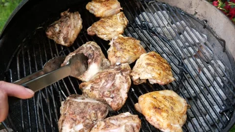Using tongs to turn chicken thighs as they cook on a charcoal grill in a ke.. Stock Footage 312111762