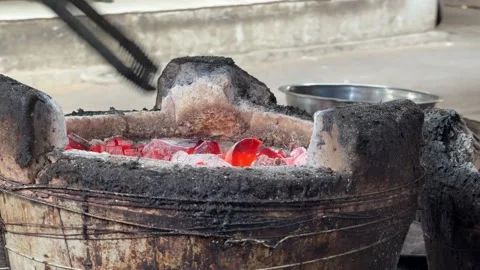 Using tongs, a vendor redistributes hot coals between clay ovens, maintaining Stock Footage 329988780